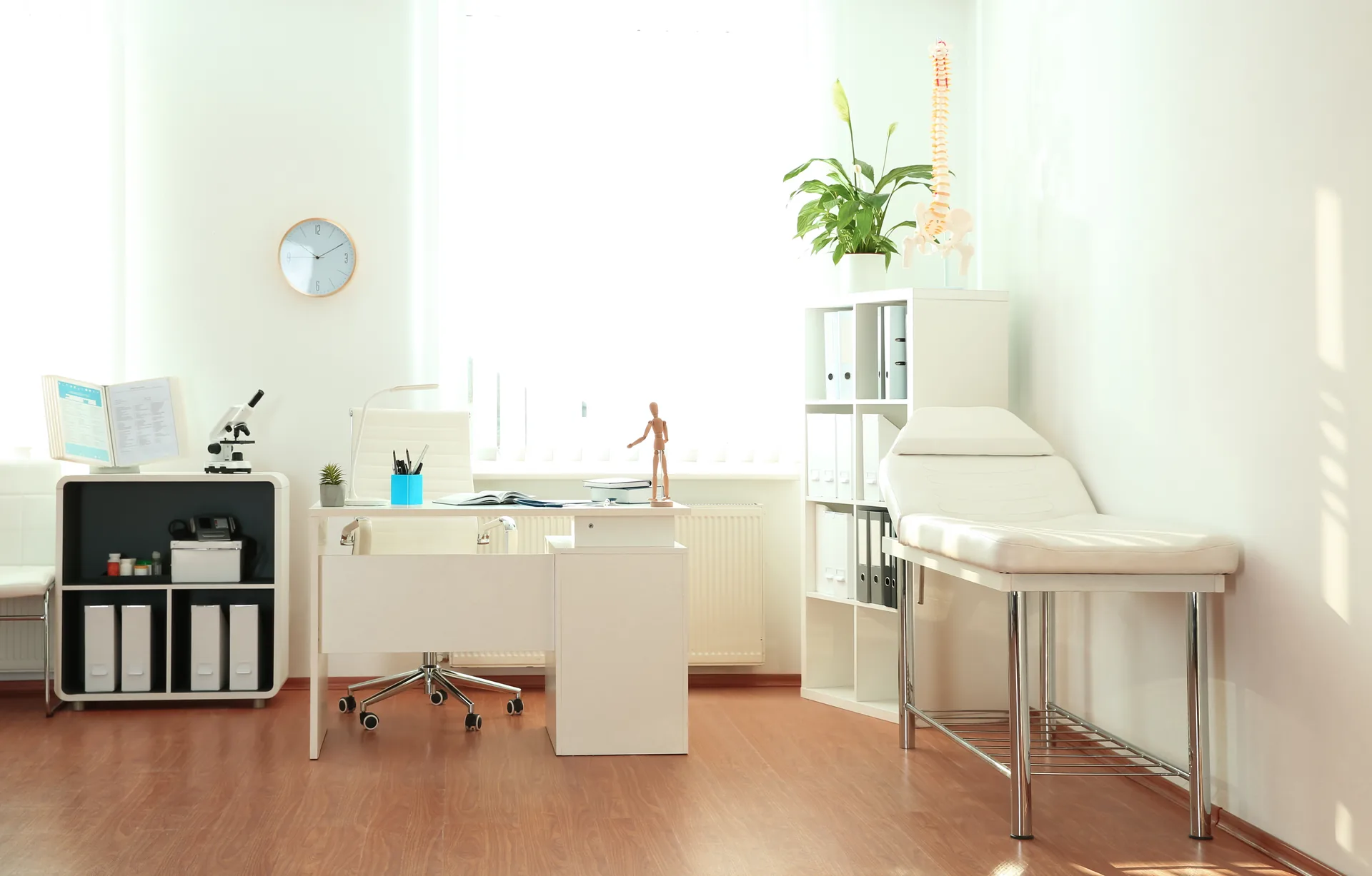 Bright modern doctor's office at Sycamore Dermatology Group with exam bed, desk, and natural light